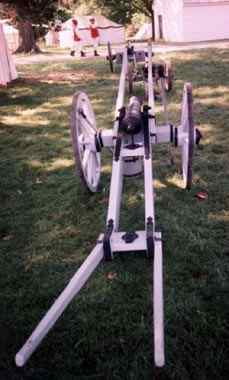 A historic cannon displayed on a grassy field with trees in the background.