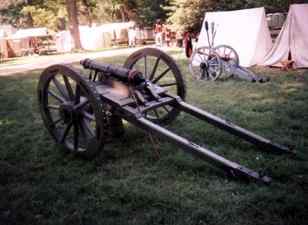 An antique cannon mounted on a wooden carriage with spoked wheels, displayed outdoors.