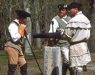 Reenactors dressed in historical military uniforms preparing a cannon.