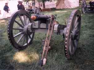 A historical reenactment scene with a vintage cannon on display, wooden wheels and metal fixtures, set on a grassy field with people dressed in period costumes in the background.