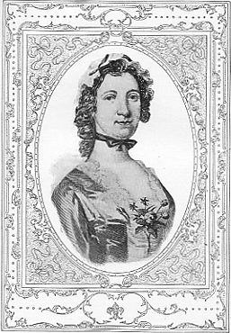 A vintage black and white portrait of a woman with curly hair adorned with a floral accessory, wearing a dress with a flower detail on the front, framed by an ornate border.